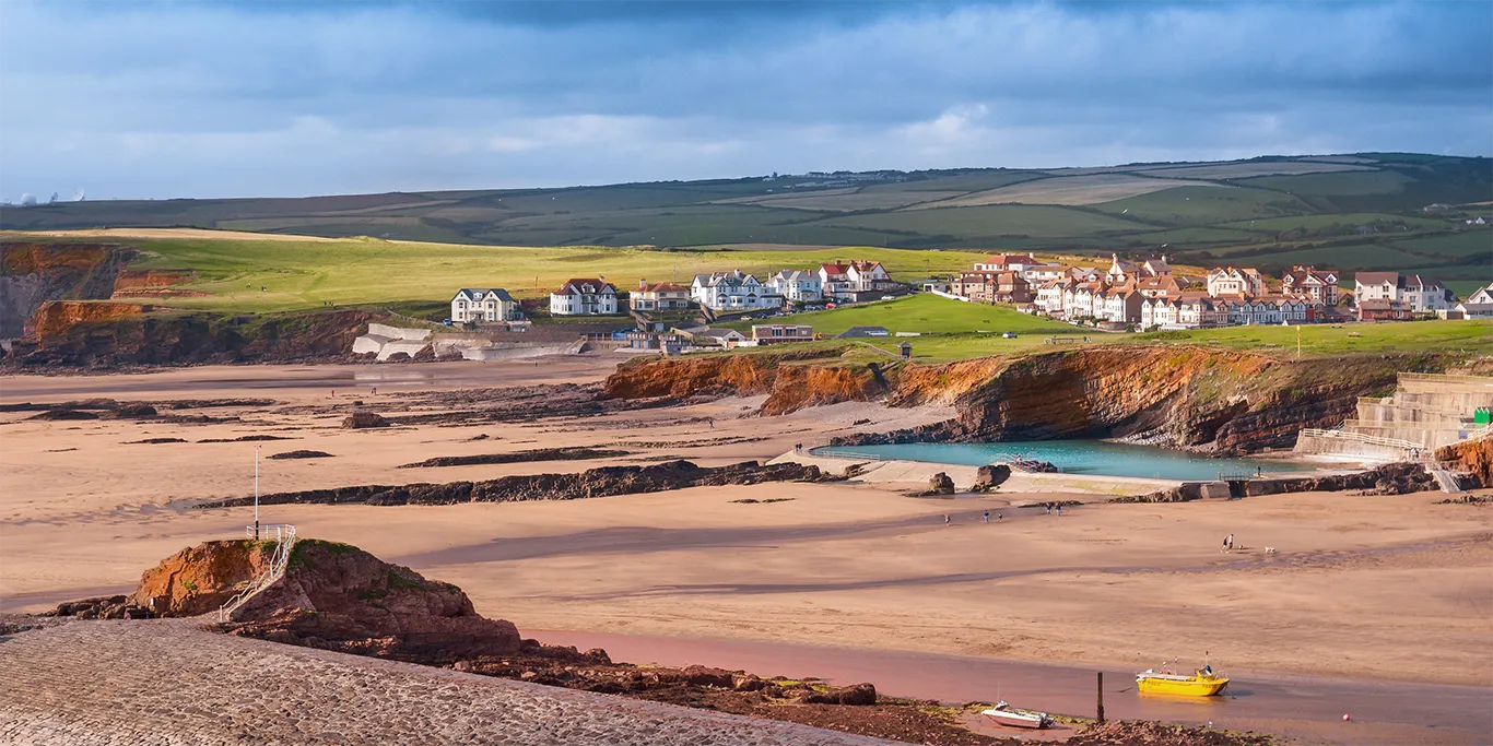 View of Bude houses from the quiet beach with the countryside stretching into the background