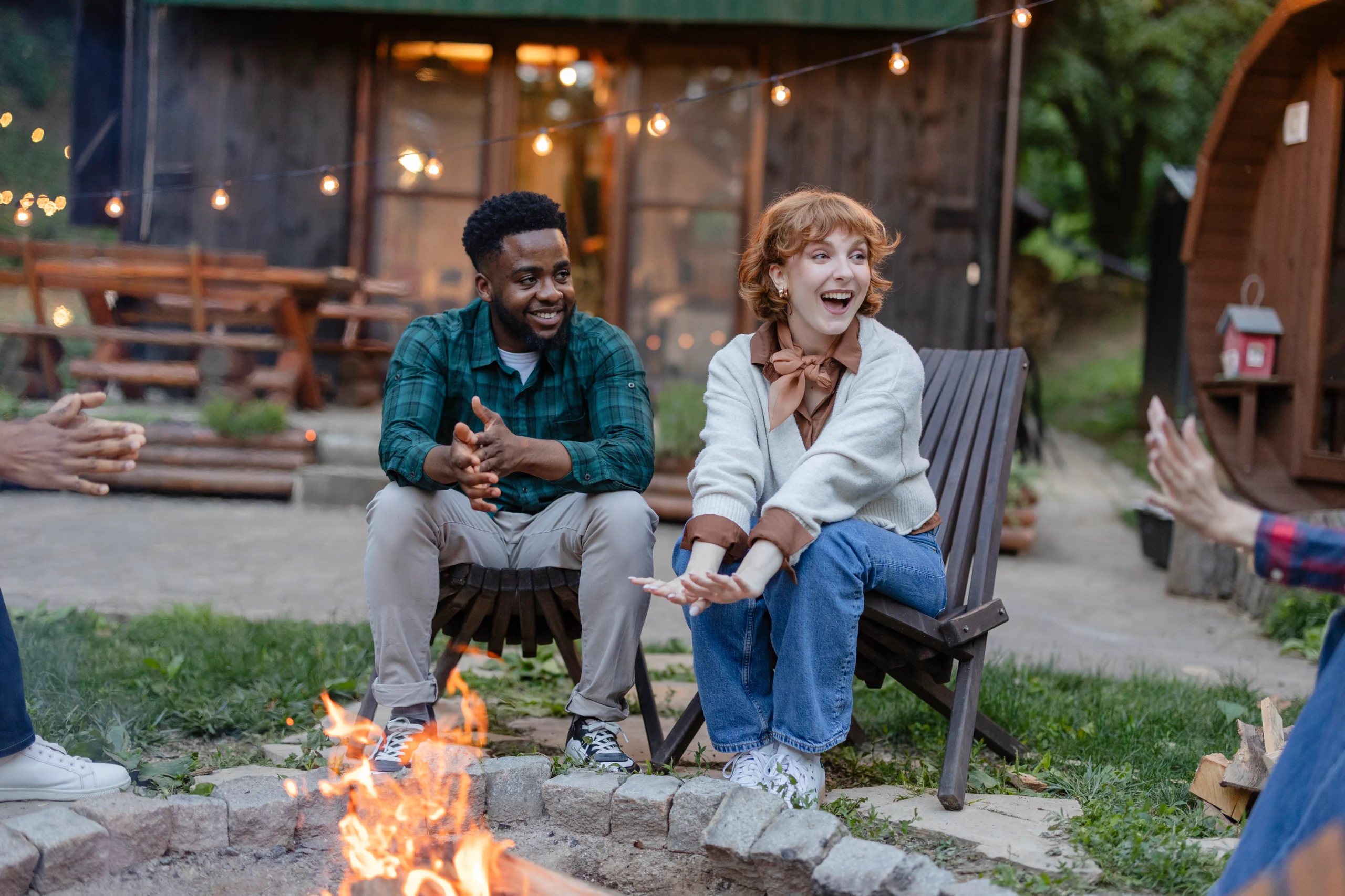 two people sitting around an outdoor campfire laughing and talking