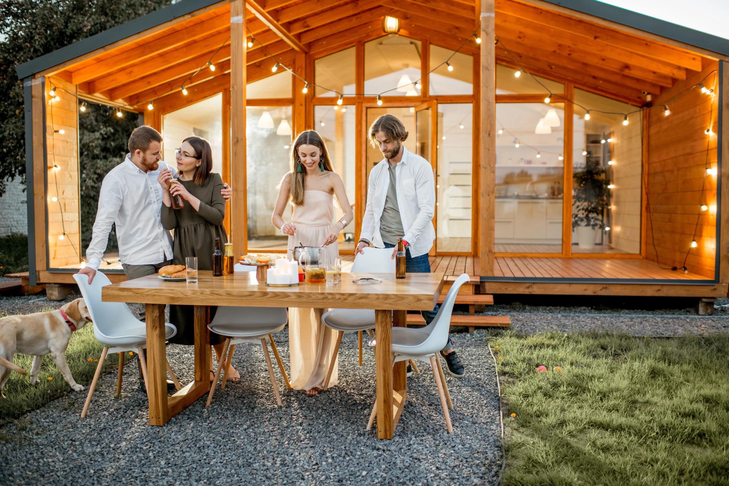 group of people standing at a table outside of a wooden cabin